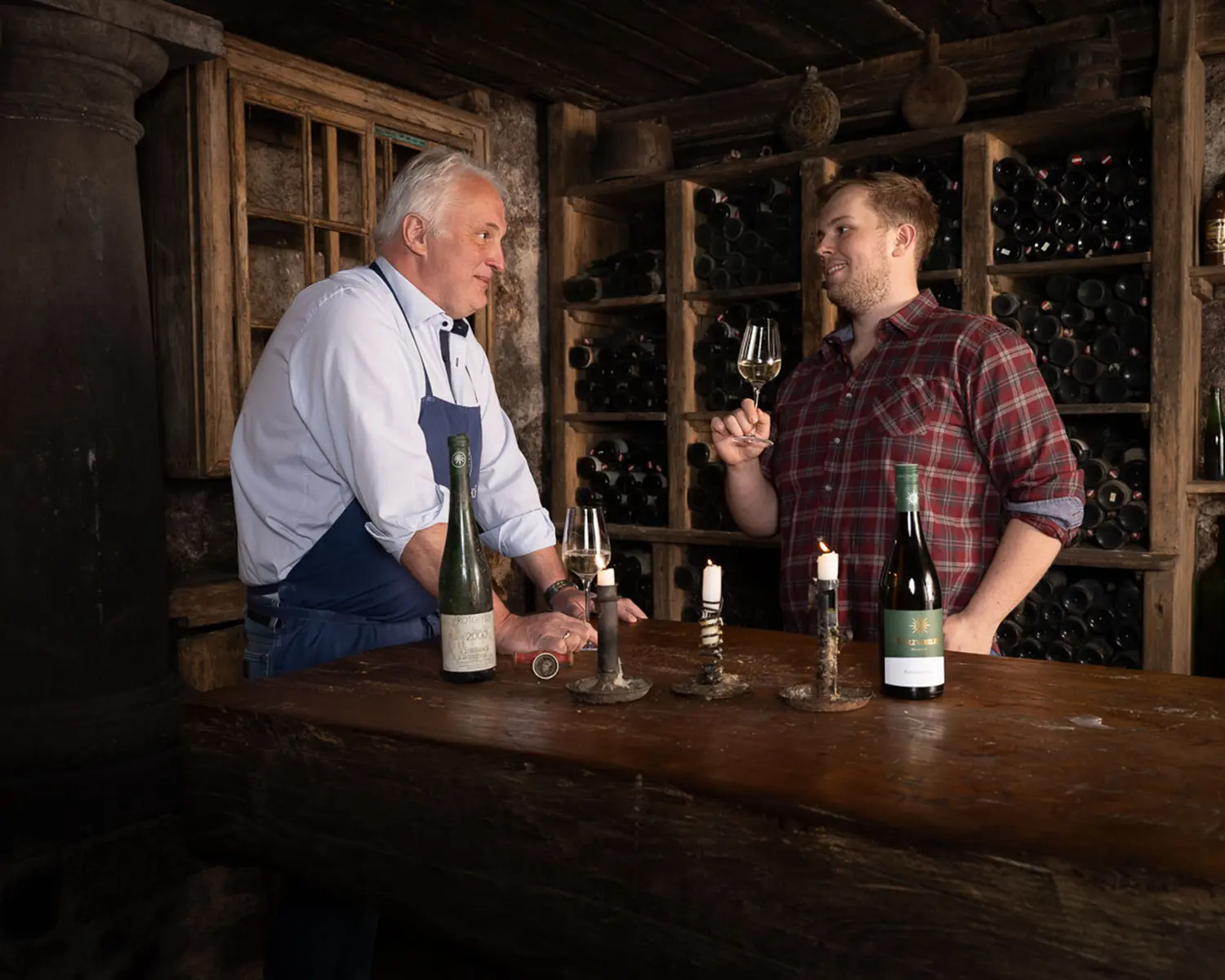 Portrait von Vater und Sohn beim Weintrinken im Weinkeller in authentischer Atmosphäre